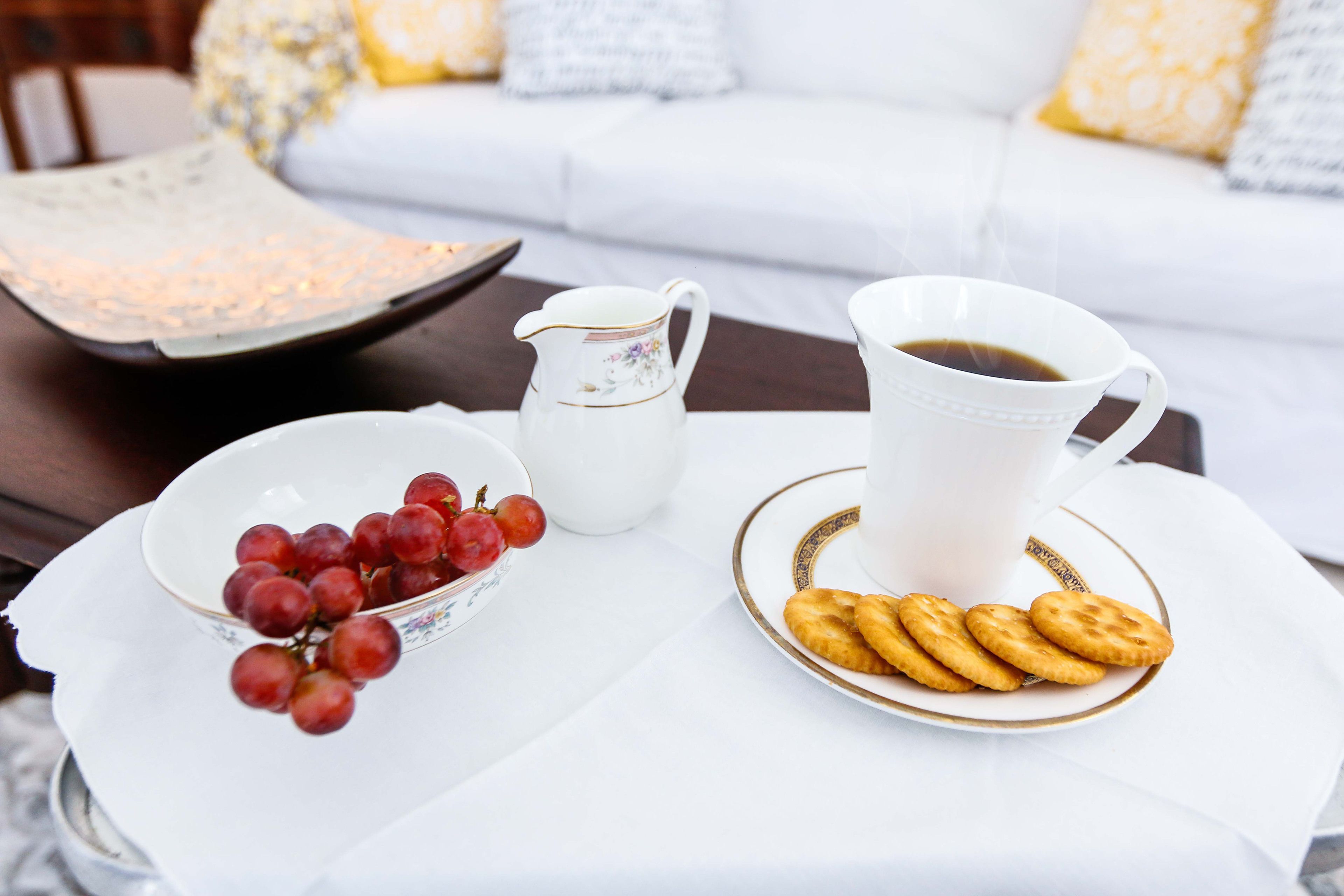 A white table with a white pitcher, a bowl of red grapes, and a plate of biscuits.