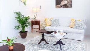 Una sala de estar con un sofá blanco, dos almohadas amarillas con estampado, una mesa de centro, una lámpara y un cuadro de un caballo.