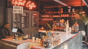 Mostrador de cafetería con un letrero de neón, carteles de menú y un barista preparando bebidas.