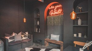 Una habitación acogedora con un letrero de neón, un sofá, un banco, una mesa y estantes con adornos.