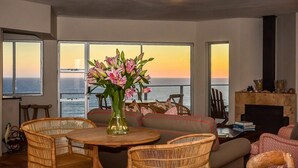 A living room with a view of the ocean, wicker furniture, a fireplace, and a vase of flowers. - Headlands House Guest Lodge (Knysna)