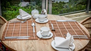 A round wooden table set for dining with white tableware, including plates, cups, and cutlery, on a bamboo mat. - Headlands House Guest Lodge (Knysna)