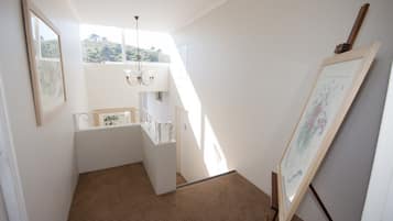 A narrow stairway with a glass railing, a chandelier, and framed artwork on the walls.