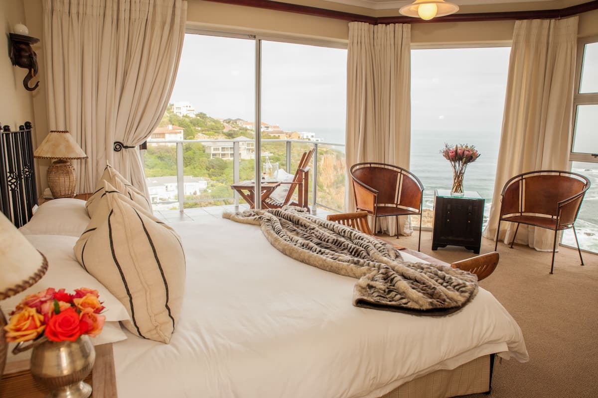 Een hotelkamer met een groot bed, uitzicht op zee en een balkon met stoelen en een tafel.