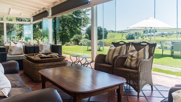 Un patio cubierto con mobiliario de mimbre, una mesa de madera y vistas a un paisaje verde.