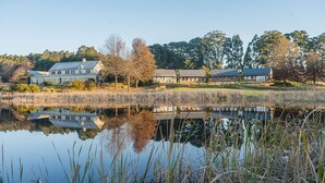 Una propiedad junto al lago con varias construcciones, incluyendo una casa grande y edificios más pequeños, rodeada de árboles y una masa de agua tranquila.