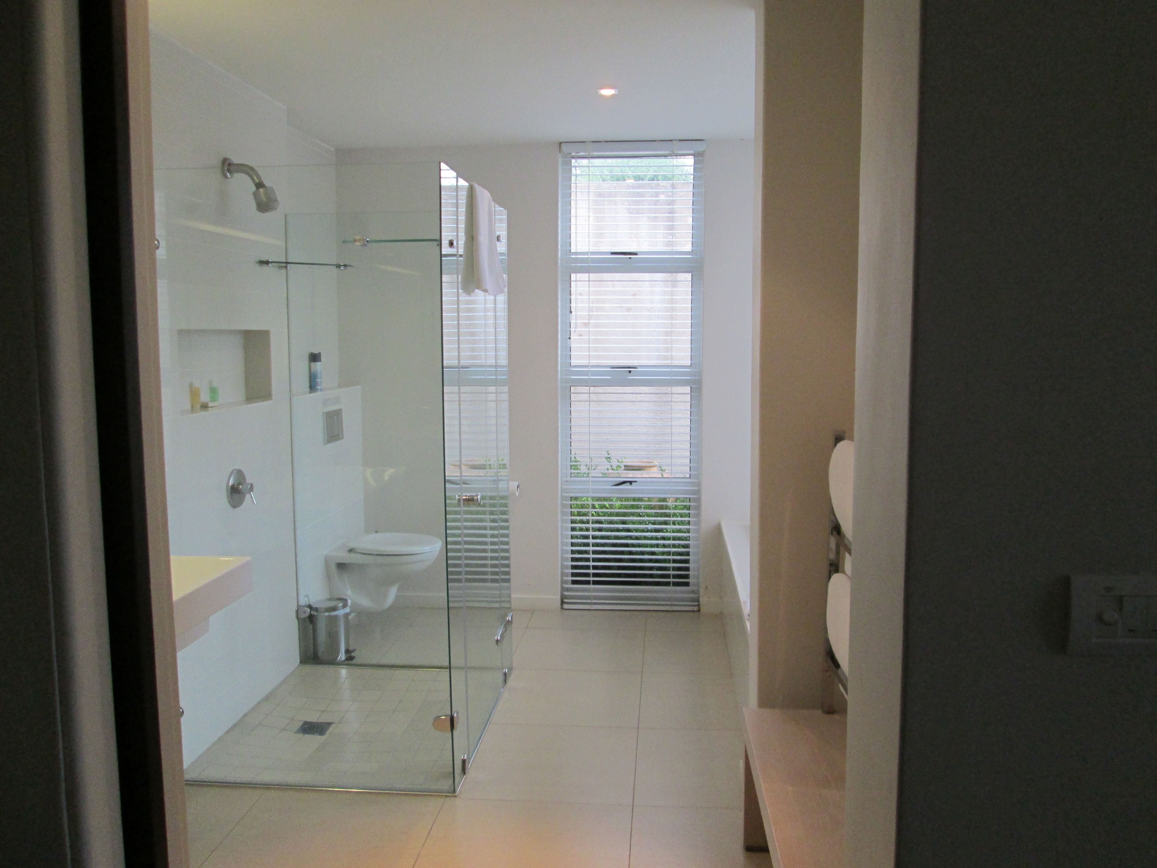 Une salle de bain moderne avec une douche à parois de verre, des toilettes et une fenêtre équipée de stores.