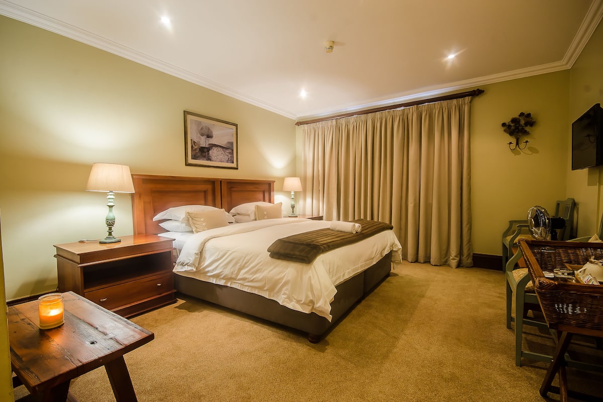 Une chambre à coucher bien rangée, avec un grand lit, des tables de chevet, une chaise et une petite table sur laquelle est posée une bougie.