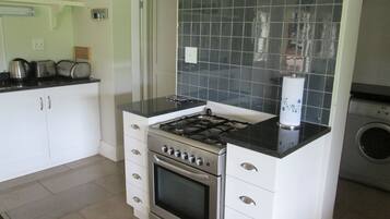 Una cucina con mobili bianchi, piano cottura a gas, forno integrato, microonde e lavatrice.