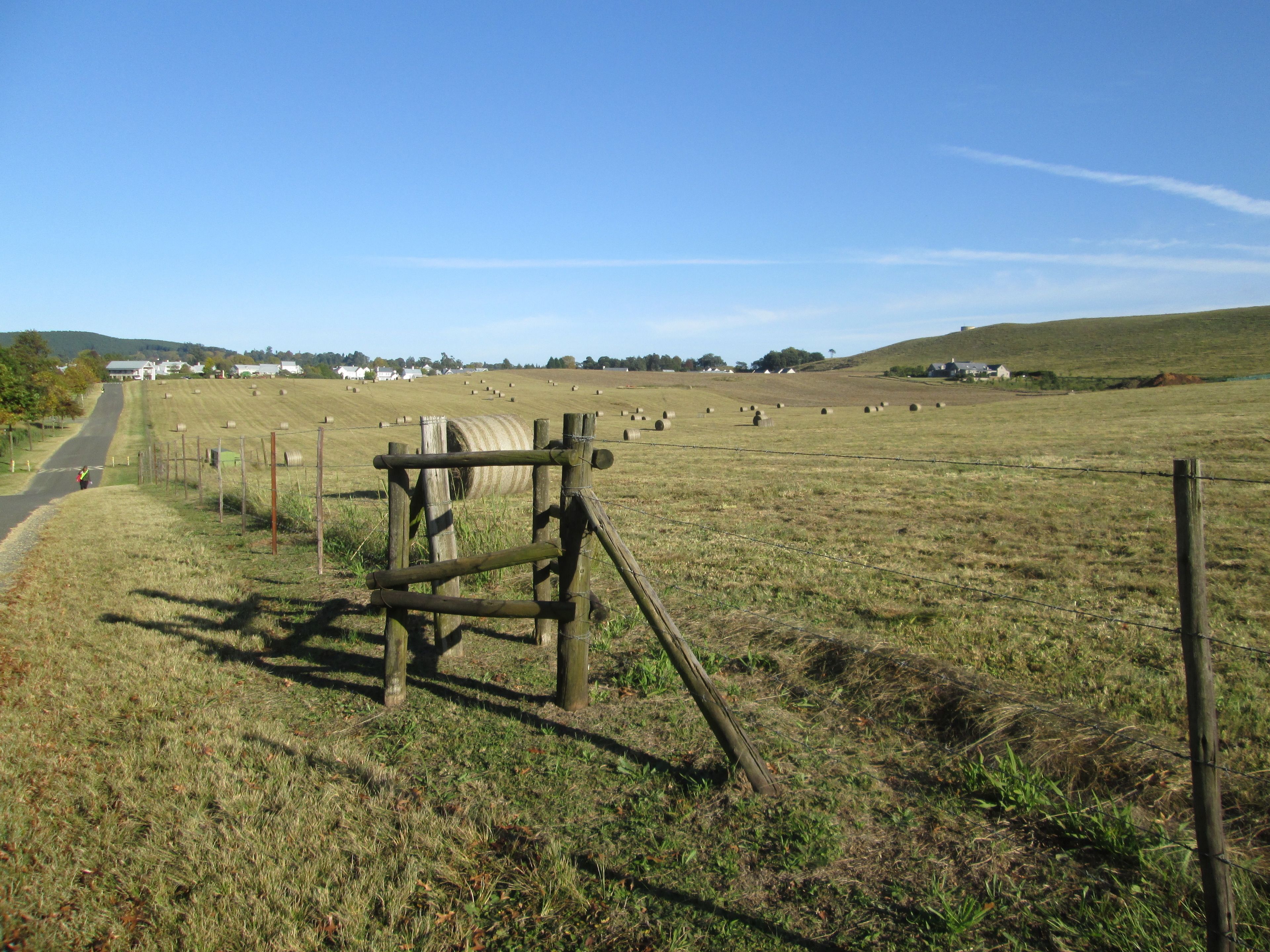 A rural landscape with a road, hay bales, and a wooden fence.