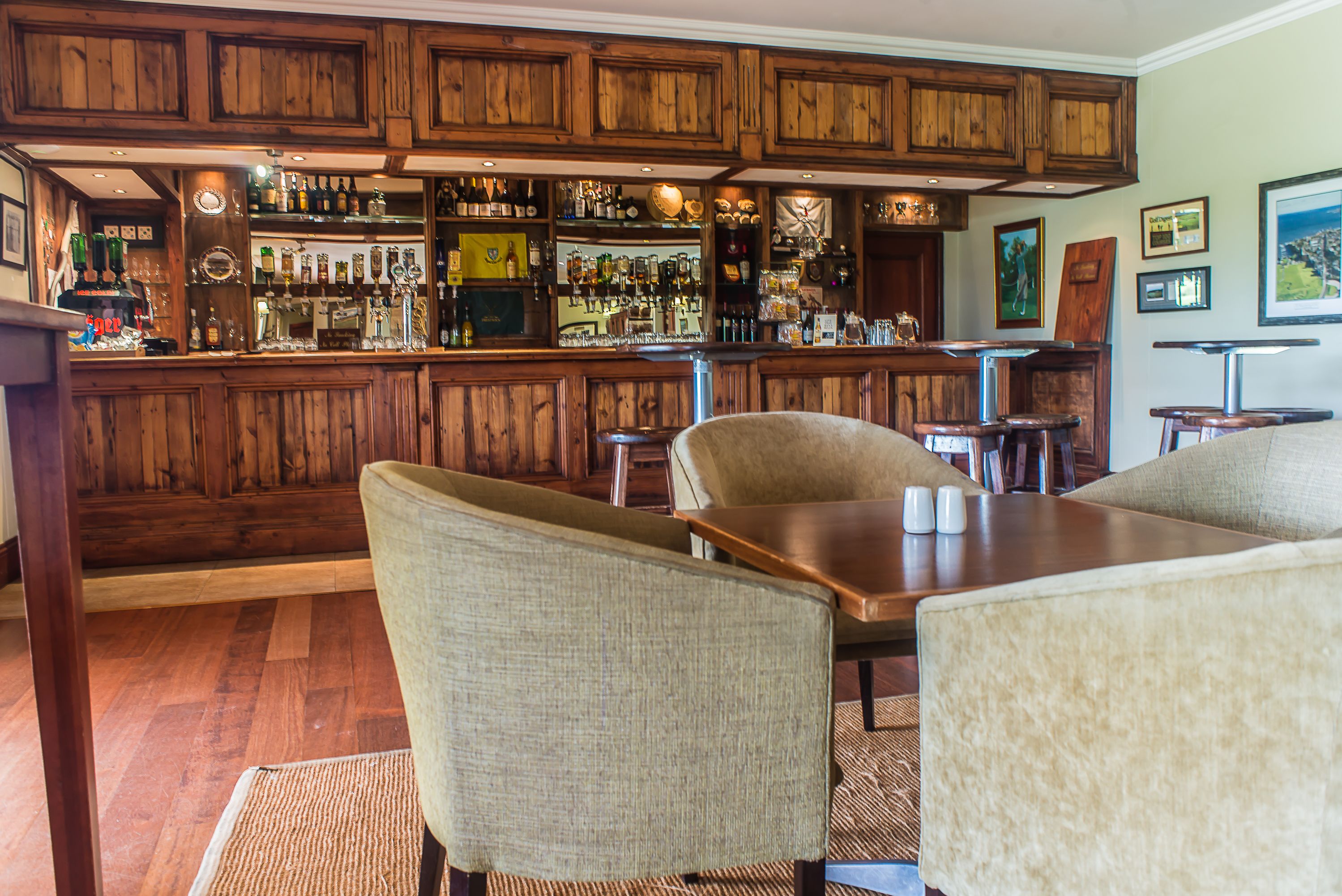 A bar area with wooden cabinets, bar stools, and a counter with various bottles and glasses.