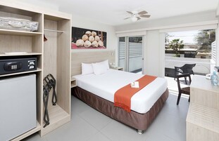 Quarto de hotel com cama, escrivaninha, cadeira, guarda-roupa e varanda com vista para um parque.