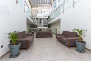 Um hall amplo com teto alto, área de estar central com sofás e plantas em vasos.