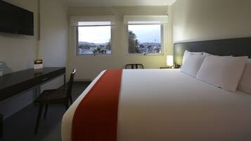 Une chambre d’hôtel avec un grand lit, un bureau et deux fenêtres donnant sur la ville.