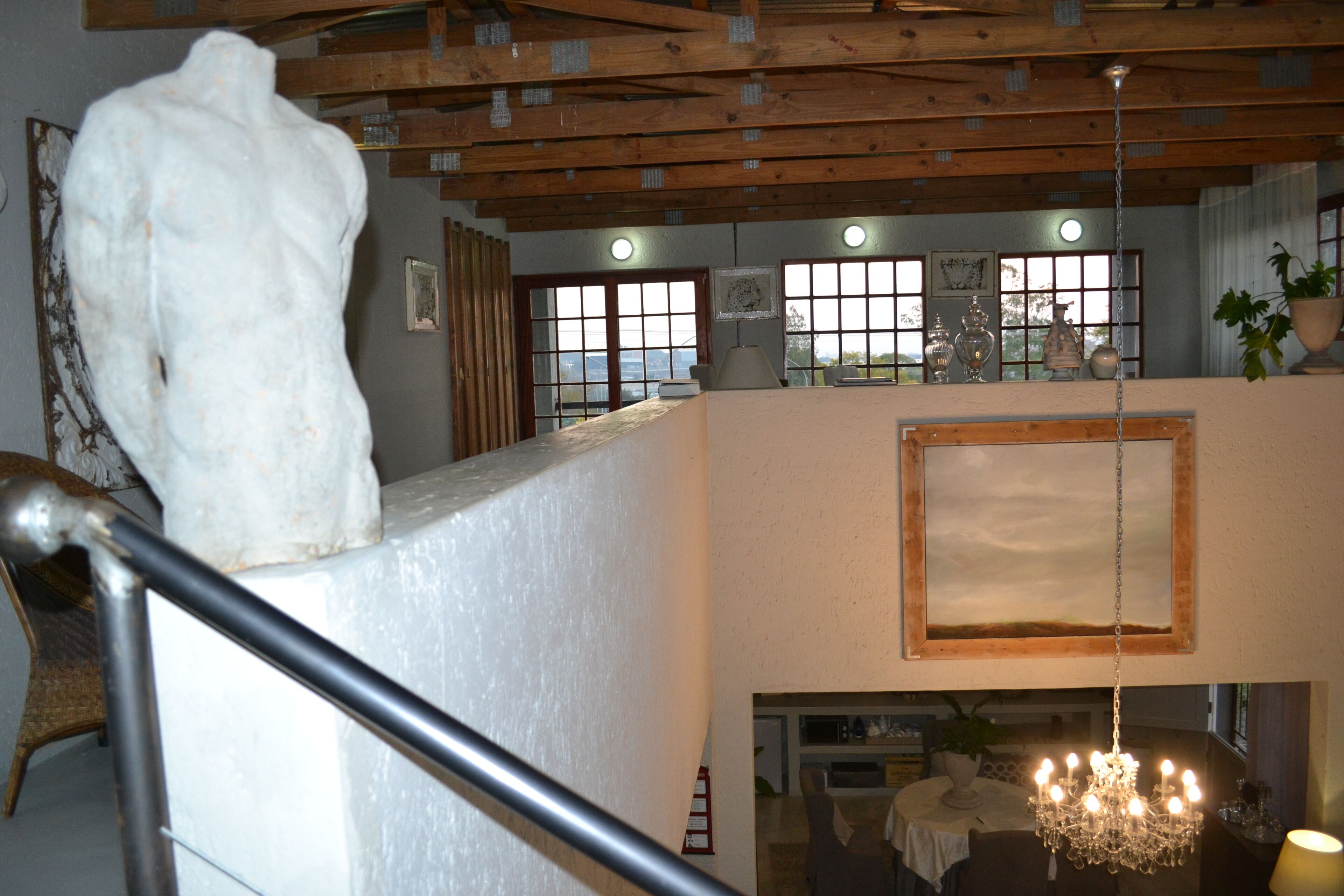 A high-ceilinged room with a wooden beam structure, a chandelier, and a large white sculpture.