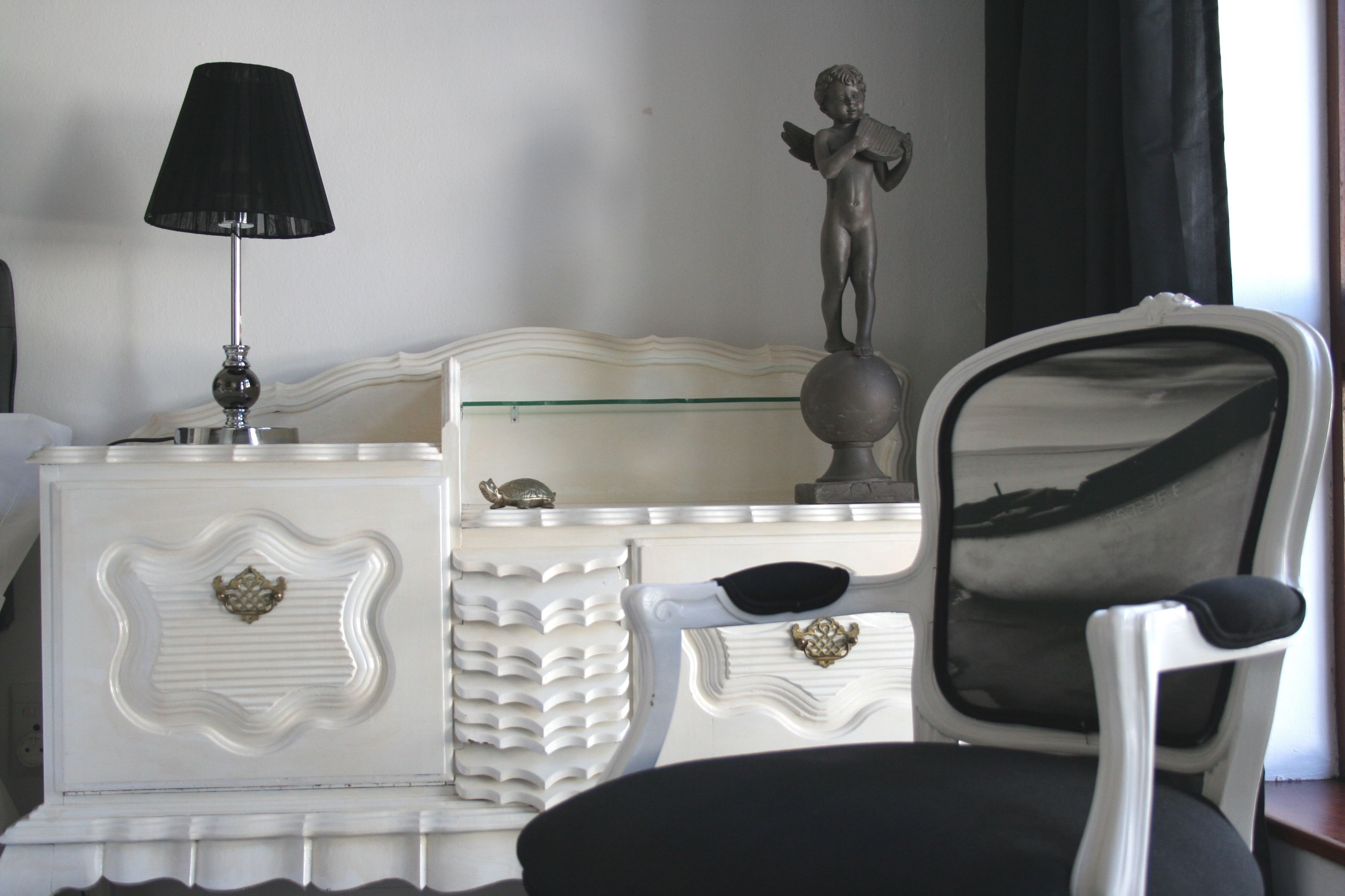 Un aparador blanco con una lámpara negra, una estatua y una silla con espejo.