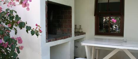 A brick oven attached to a white wall, a window with a wooden frame, and a white bench.