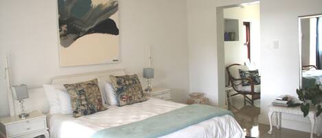 A bedroom with a bed, nightstands, a lamp, a painting, a chair, a table, and a mirror.