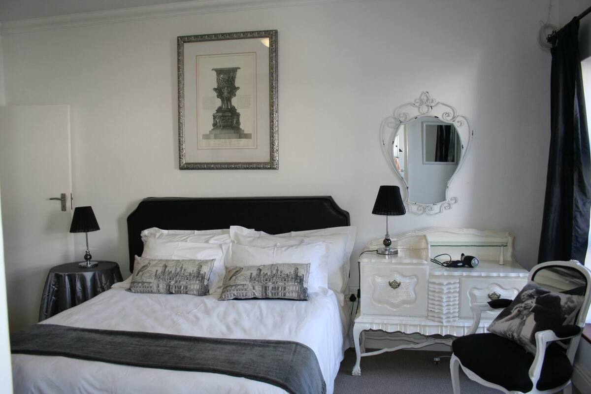 Ein Hotelzimmer mit Bett, Kommode, Stuhl, Spiegel und einem gerahmten Bild an der Wand.