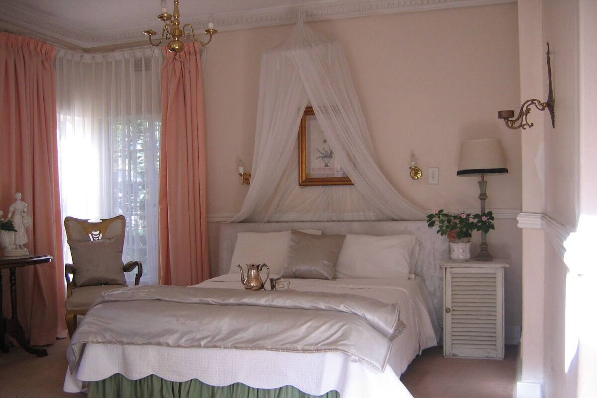 Un dormitorio con una cama grande, una mesita de noche con lámpara, una silla y un adorno en la pared.