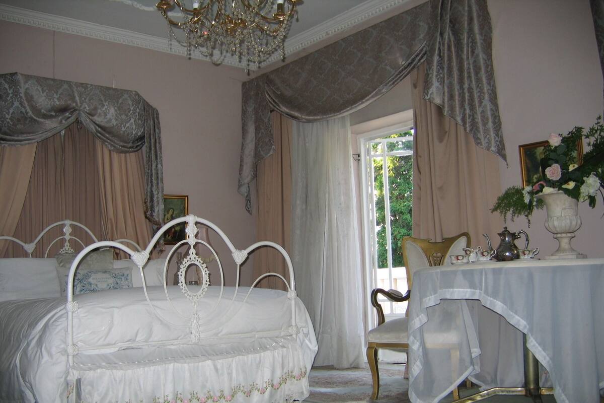 Un dormitorio con una cama blanca ornamentada, una mesa con un jarrón de flores y una silla.