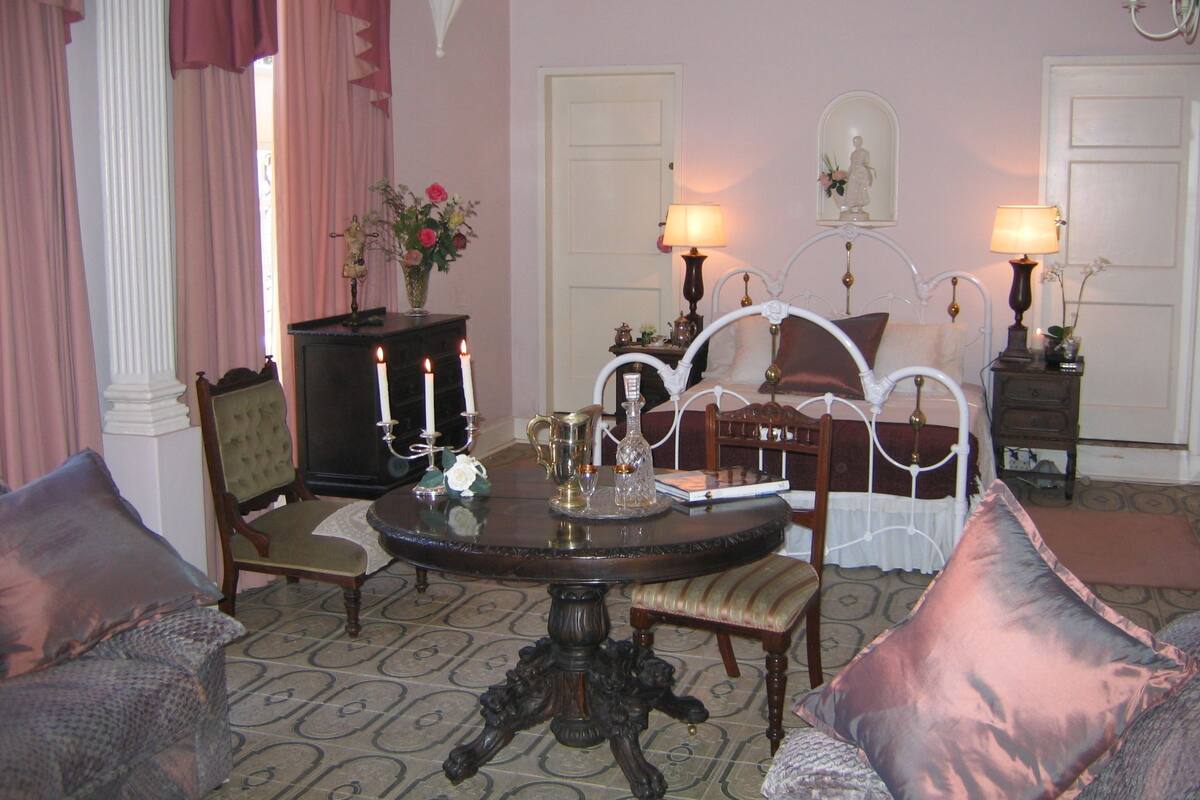 Una habitación con una mesa redonda, dos sillas, una cama con dosel y un aparador con espejo.