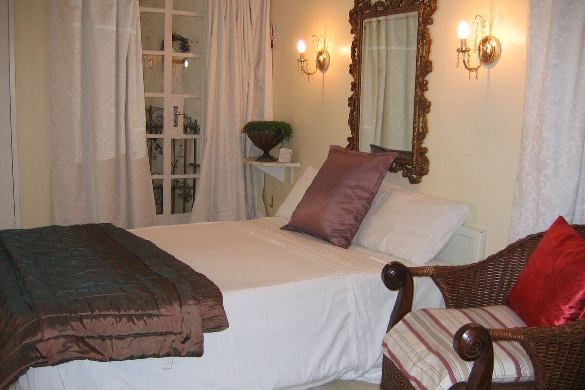 Un dormitorio con una cama, una silla, un espejo y una ventana con cortinas.
