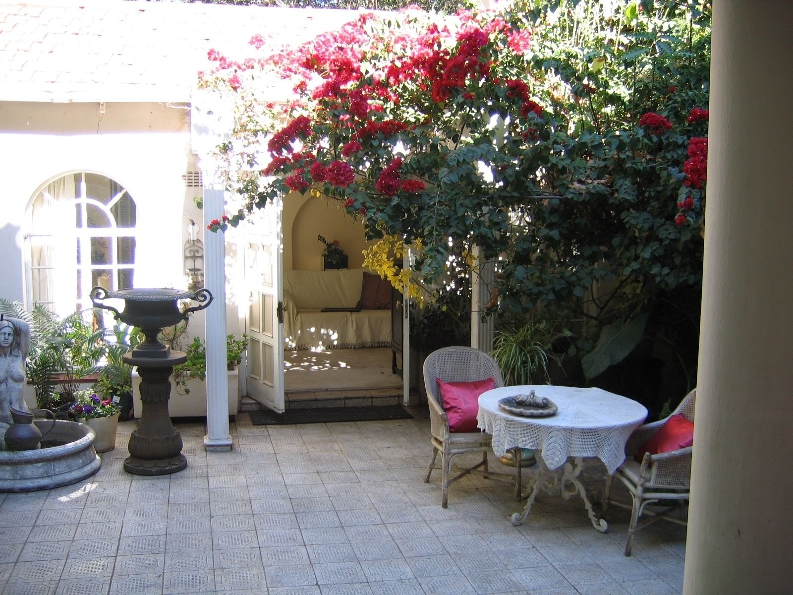 Un patio con una mesa y sillas, una estatua y una planta floreciente grande.