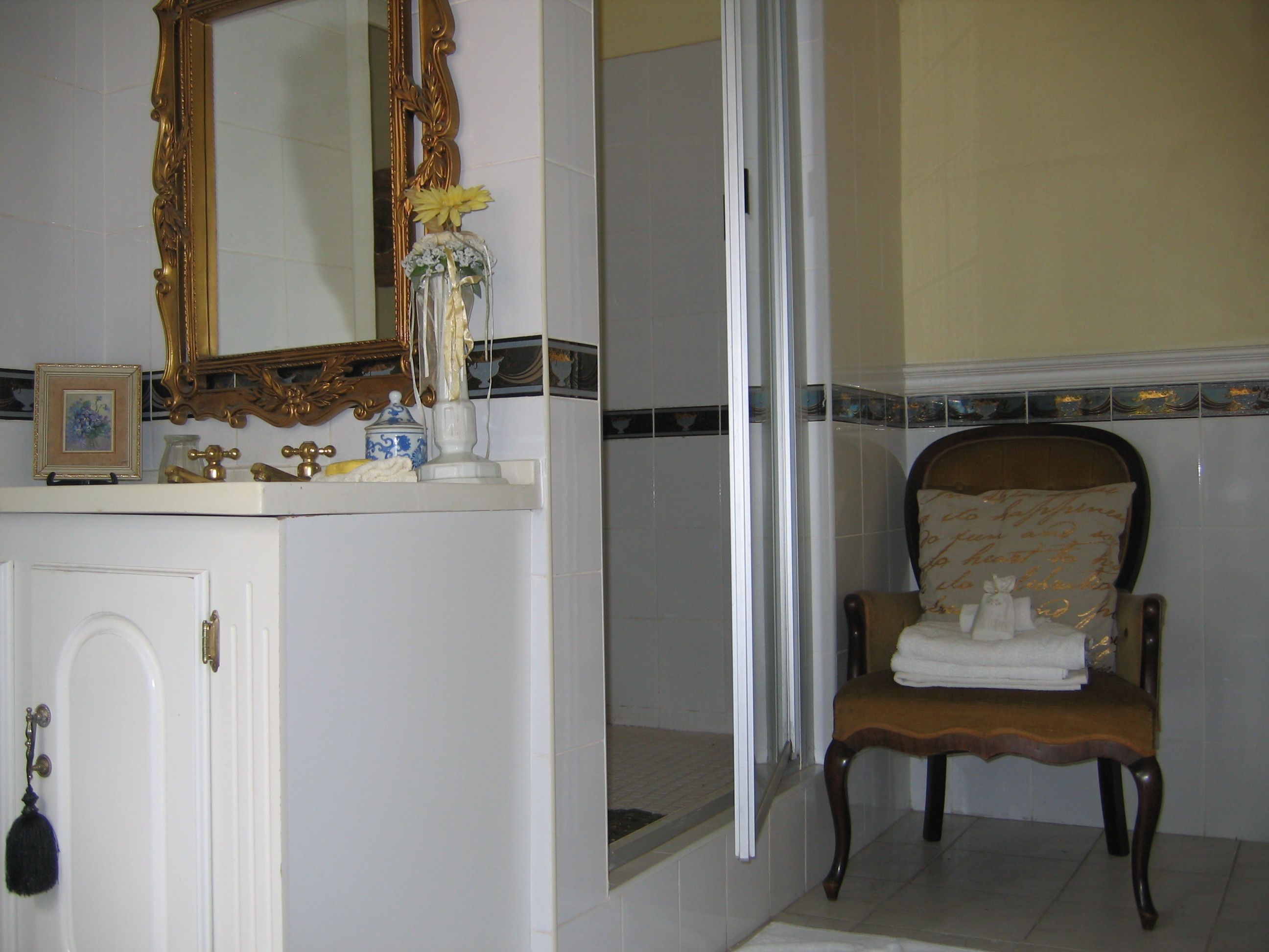 Un baño con tocador, espejo, silla con toallas y zona de ducha.