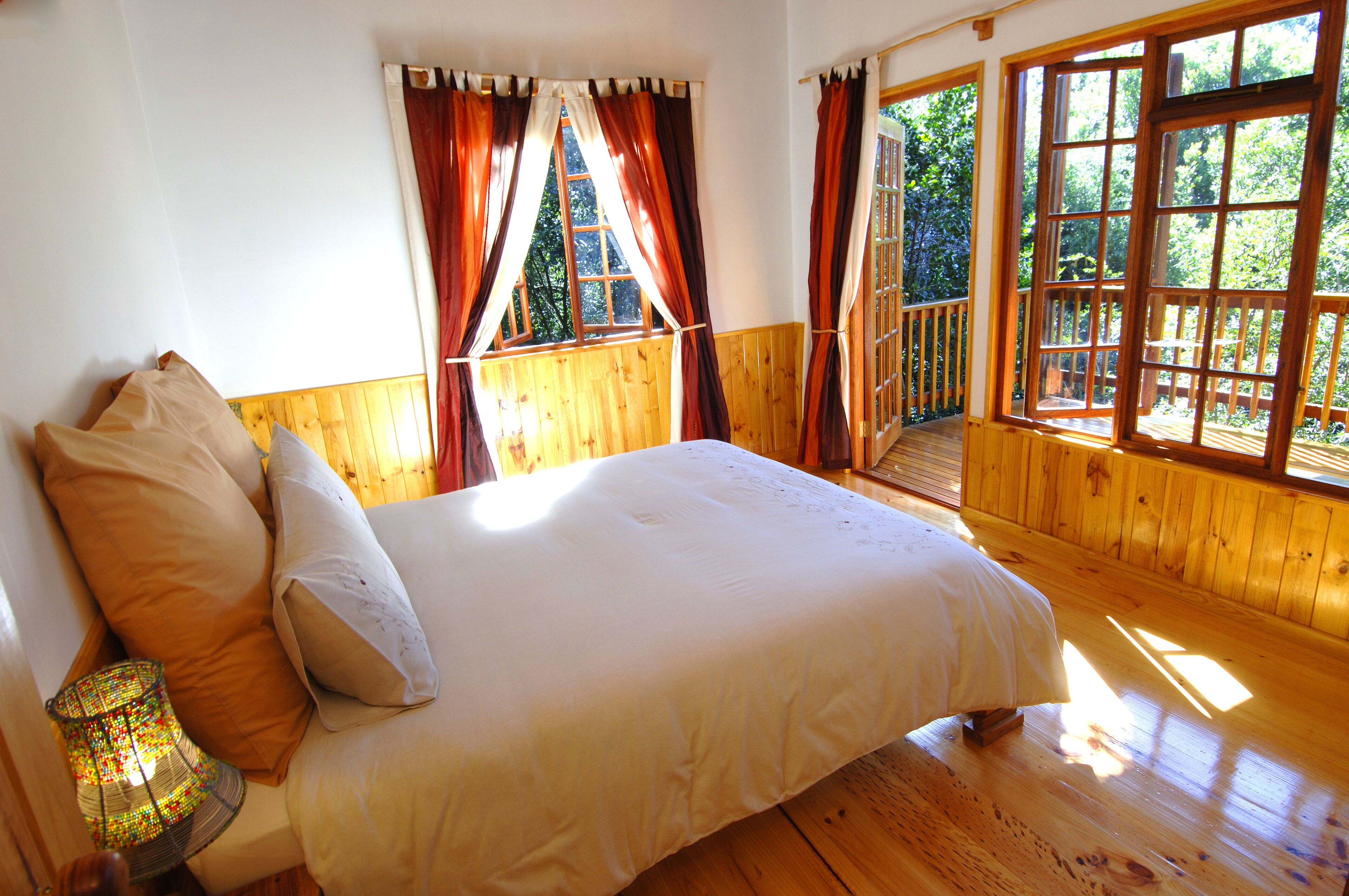 A bedroom with a wooden floor, a bed with white bedding, and a window with curtains.