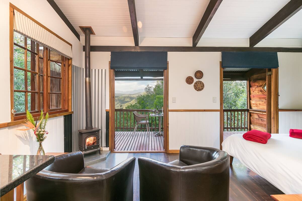 Una habitación con chimenea, cama, balcón con vistas y comedor con sillas.