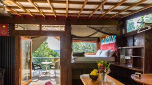 A cozy room with a wooden ceiling, a bed with pillows, a dining table with a vase of flowers, and a view of the outdoors. - Moon Shine on Whiskey Creek (The Crags)