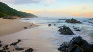 A beach with a sandy shore, rocky outcrops, and a hilly landscape in the background. - Moon Shine on Whiskey Creek (The Crags)