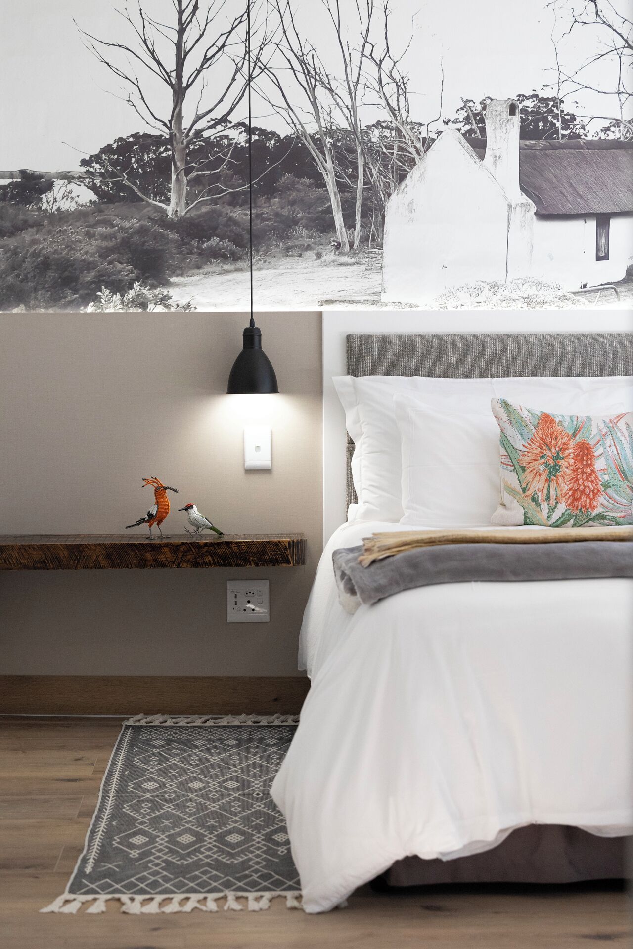 A bedroom with a bed, a hanging light, a shelf with decorative birds, and a patterned rug.