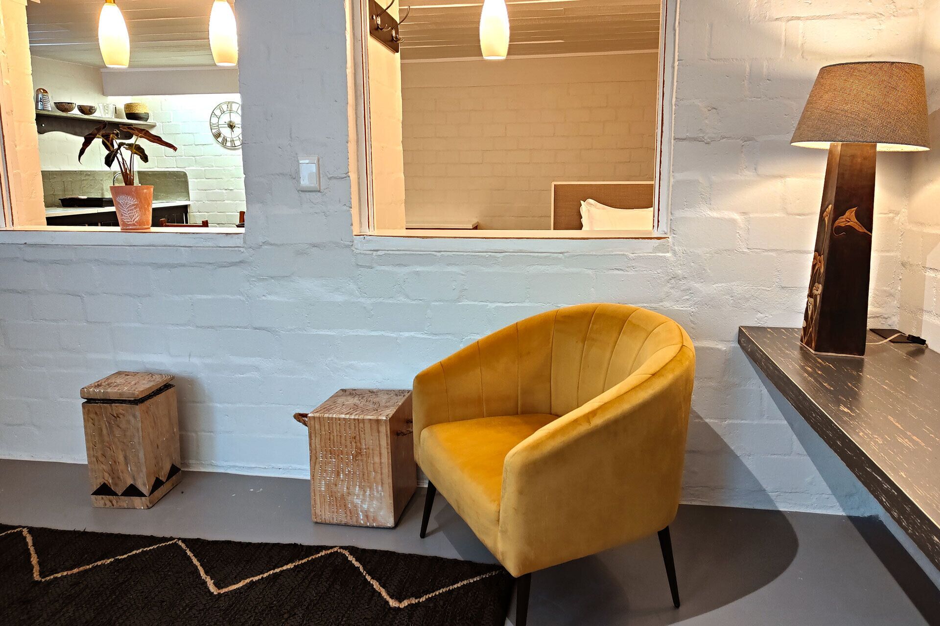Een modern interieur met een gele fauteuil, houten krukken, een lamp en uitzicht door een raam.