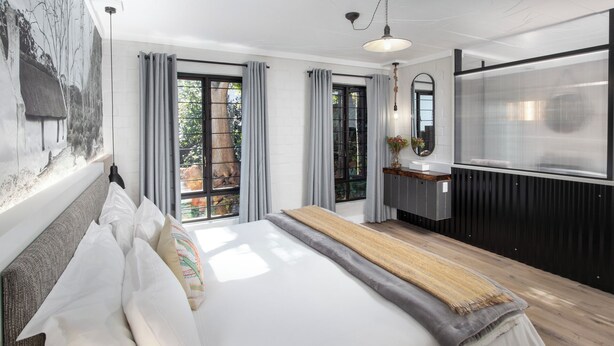 Een moderne slaapkamer met een groot bed, een houten bankje en uitzicht op de omgeving via een schuifdeur.