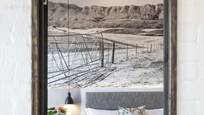 Een slaapkamer met een groot bed, een blauwe stoel, een nachtkastje met een lamp, en een muurschildering van een berglandschap.