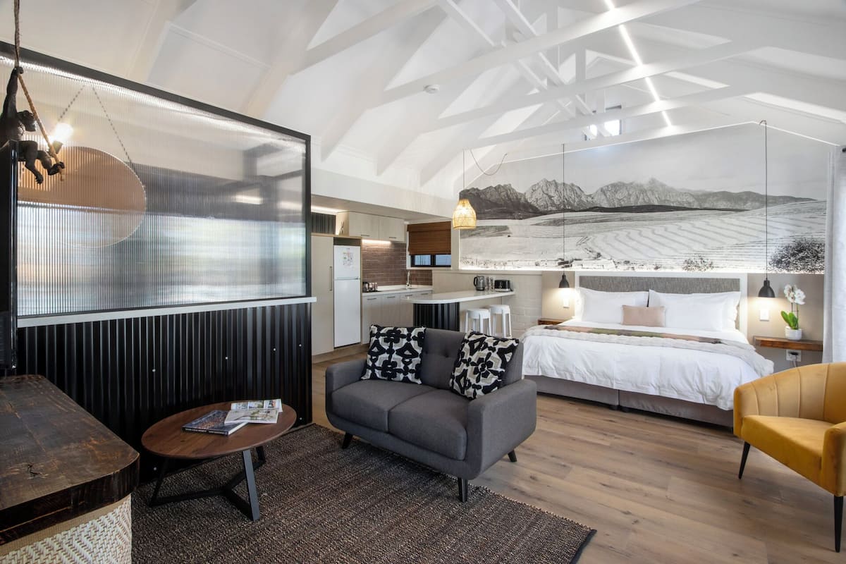 A modern interior with a large bed, a sofa, a dining area, and a kitchen.