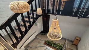 Een trap met een zwarte leuning, een geweven lamp en een plantje op de overloop.