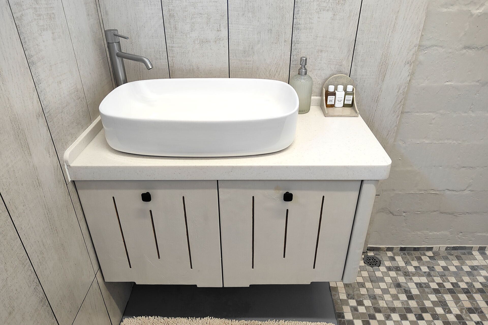 Un baño con lavamanos blanco, grifo y dispensador de jabón en la encimera.