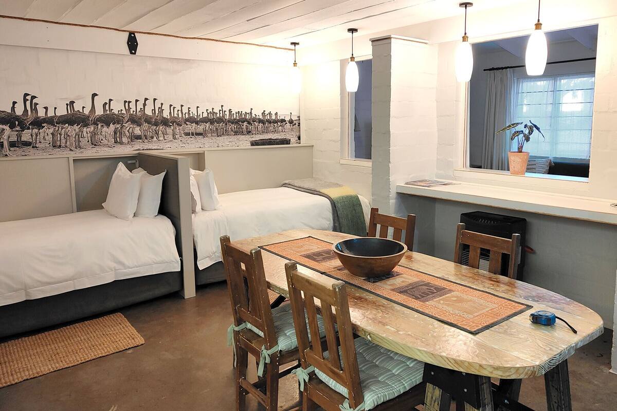 A compact room with two beds, a dining table with chairs, and a window with a view of the outside.