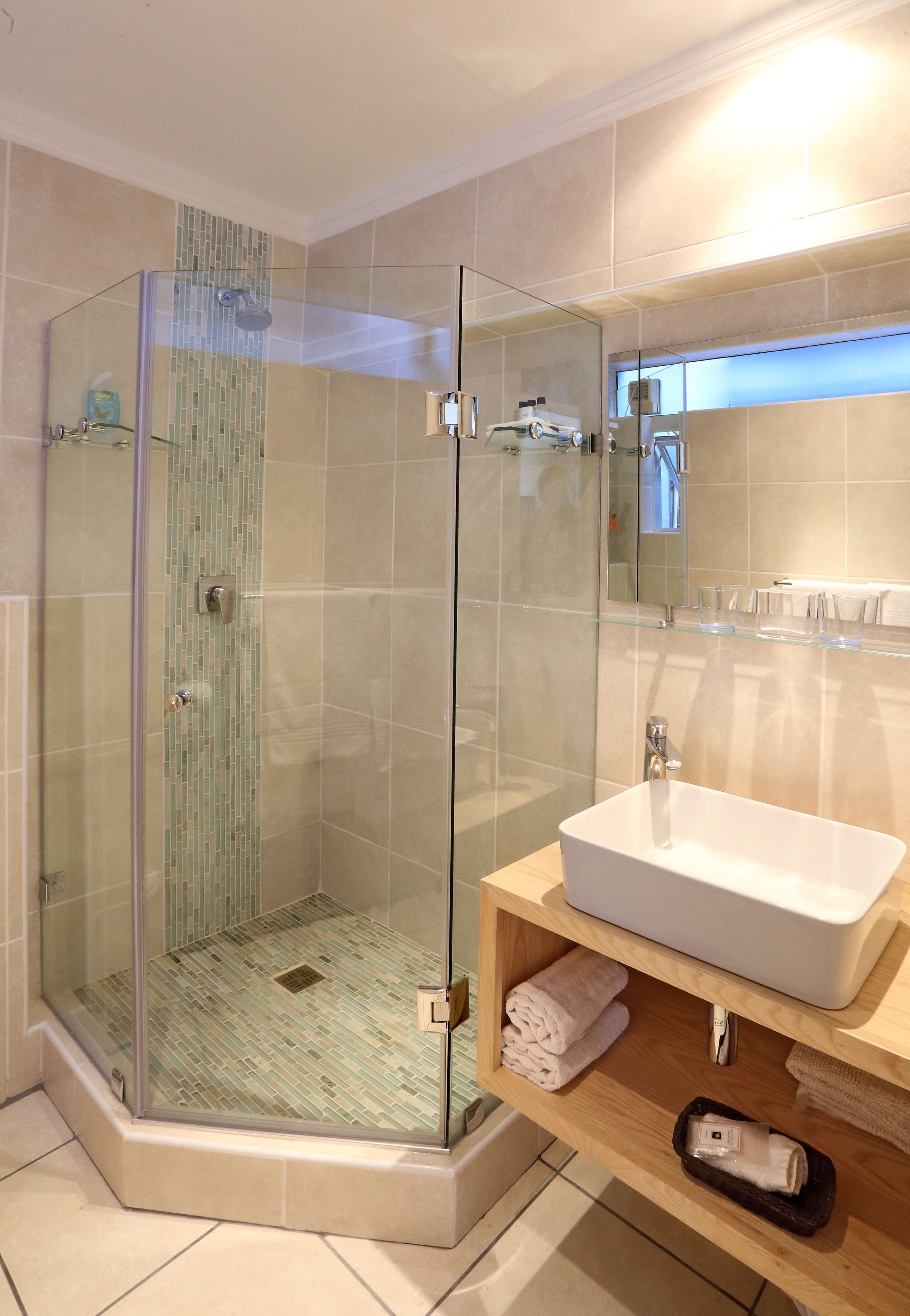 Un baño moderno con ducha envuelta en vidrio, lavamanos blanco y tocador de madera.