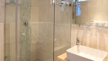 Un baño moderno con ducha envuelta en vidrio, lavamanos blanco y tocador de madera.