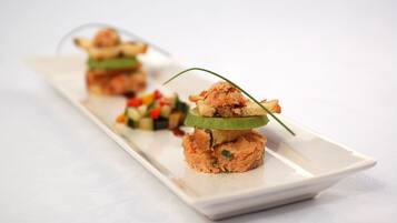 A white rectangular plate with three stacked food items, each with a slice of cucumber on top.