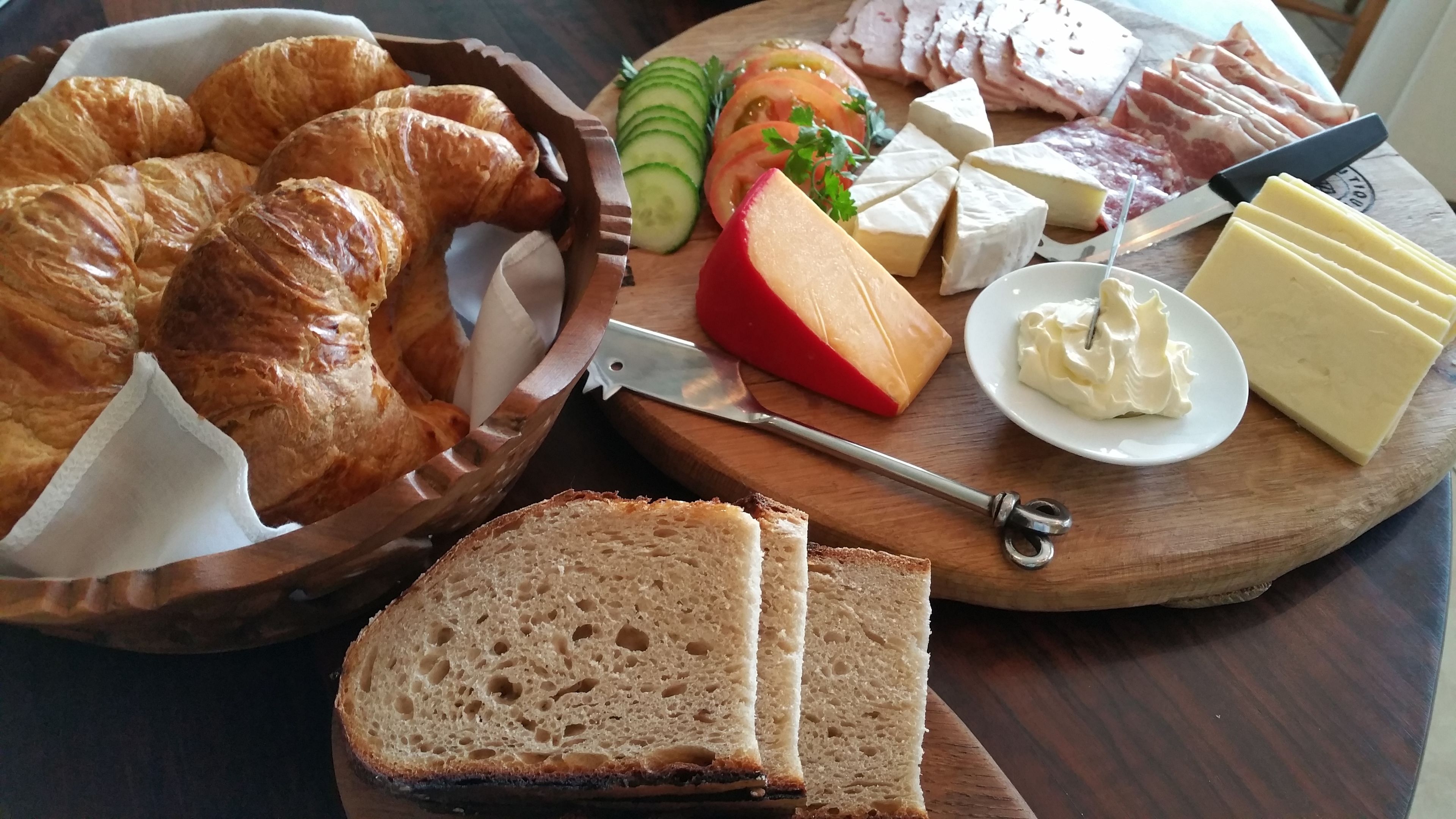 A variety of food items including croissants, cheese, and sliced bread on a wooden board.