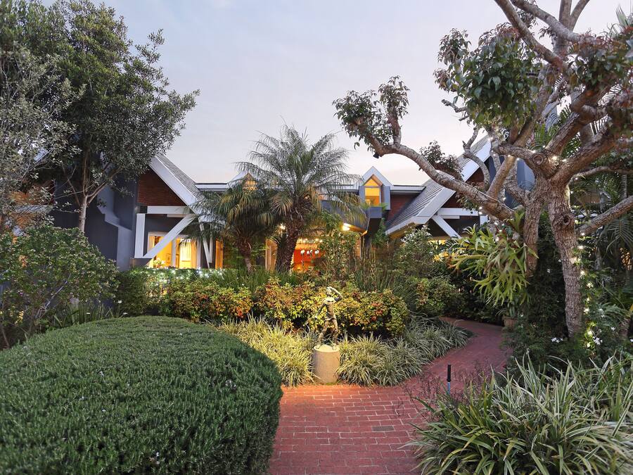 Un edificio moderno con un sendero de ladrillo que conduce a la entrada, rodeado de exuberante vegetación y un jardín bien cuidado.