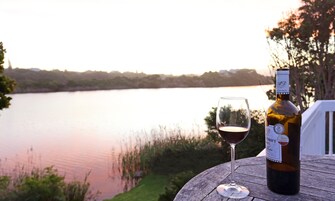 Una botella de vino y una copa sobre una mesa de madera con vista a un lago.