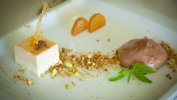 Un piattino con un cubo di dolce bianco, un dolce al cioccolato rotondo, fette d'arancia e foglie verdi.
