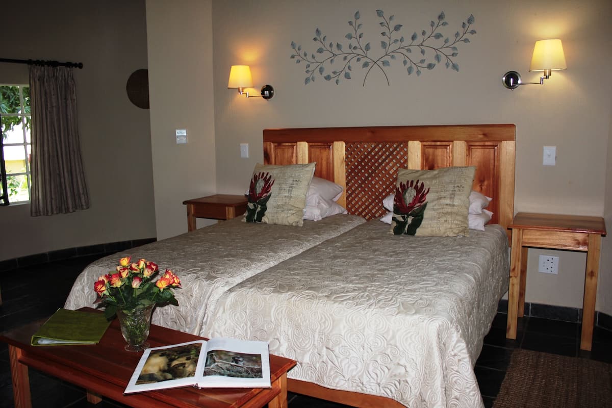 A double bed with a wooden headboard, two bedside tables, a nightstand, a bedside lamp, a vase with flowers, and a book on a wooden table.