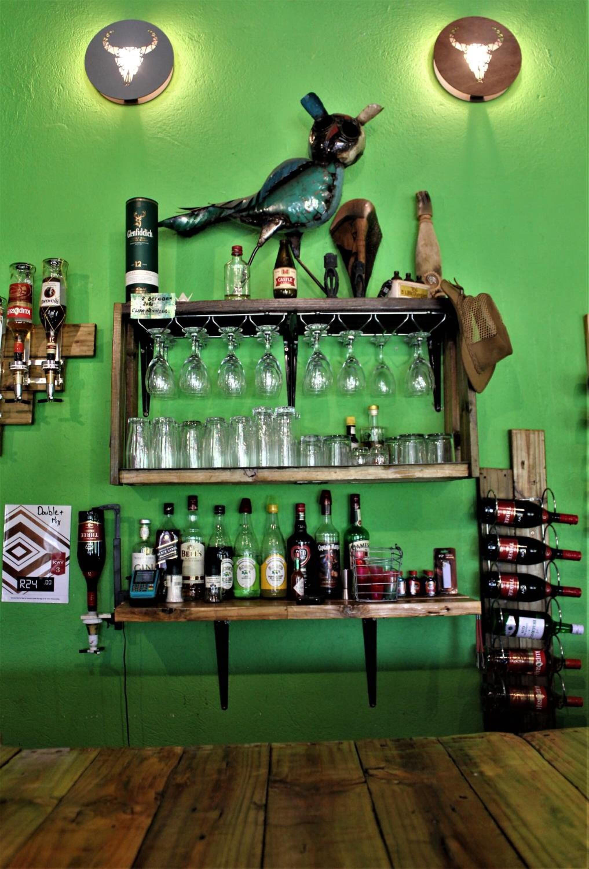 A bar with shelves of bottles and glasses, a wooden floor, and a green wall.